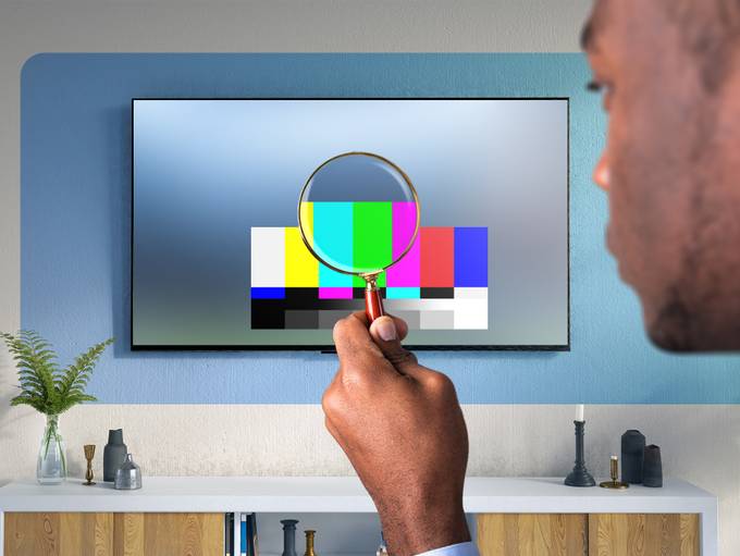 A man looking at a TV while holding a magnifying glass.