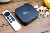 An Apple TV remote and box sit on a wood table next to popcorn.