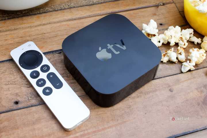 An Apple TV remote and box sit on a wood table next to popcorn.