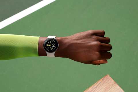 The Google Pixel Watch 3 on a wrist held above a green tennis court. 