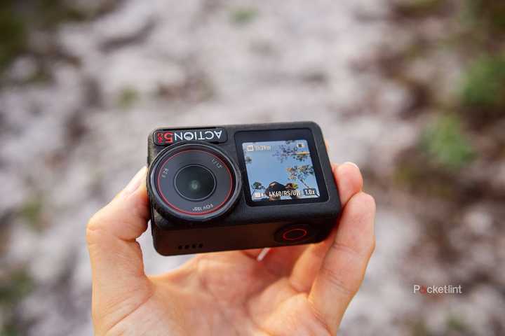 A hand holds the DJI Osmo Action 5 Pro over a sandy trail. 