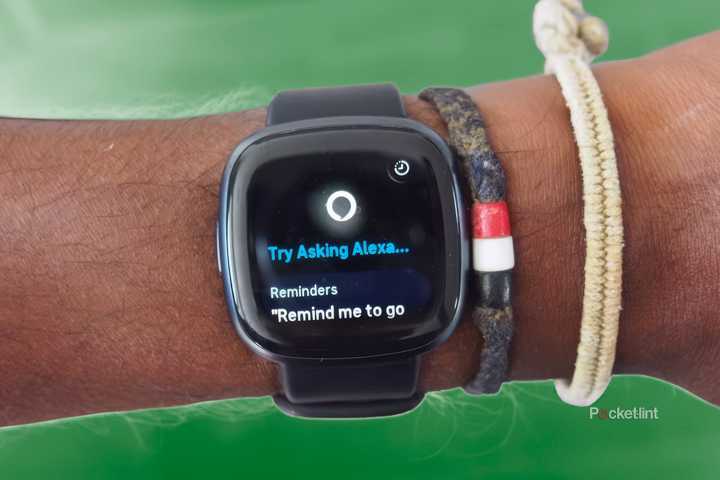 The Fitbit Versa 4 on a wrist with bracelets above a green background. 