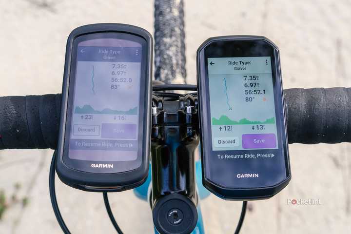 The Garmin Edge 1040 Solar and Garmin Edge 1050 are mounted to bike handlebars above a sandy road. 