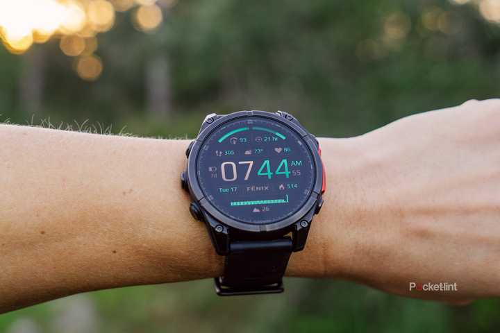 A wrist with the Garmin Fenix 8 on is held in front of a blurred forest. 