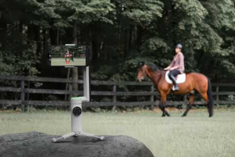 The Insta360 Flow Pro with an iPhone sits on a rock with a person on a horse in the background.
