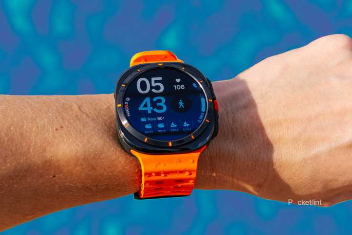 The Samsung Galaxy Watch Ultra is on a wrist held in front of a blurred blue background. 