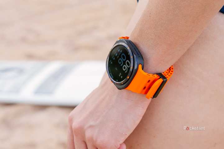 The Samsung Galaxy Watch Ultra on a wrist that rests on a leg while they stand on a beach. 